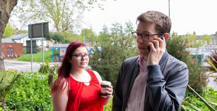 two people standing, one with phone to his ear two people standing, one with phone to his ear