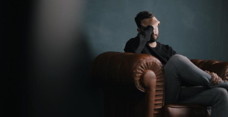 Man sitting on couch with head in his hand Man with head in