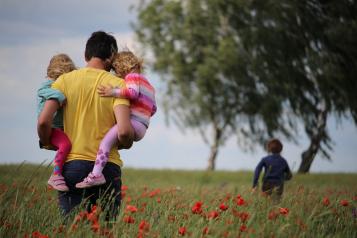 Father walking in park with kids in his arms